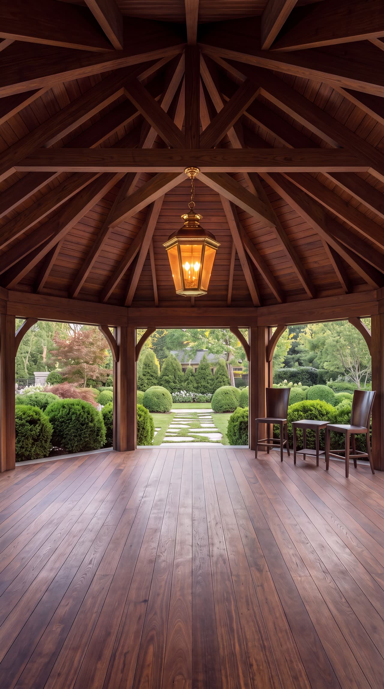 Inside the timber pavilion, looking up at rafters that meet at a hanging lantern in the centre, with arched openings on every side facing the garden.